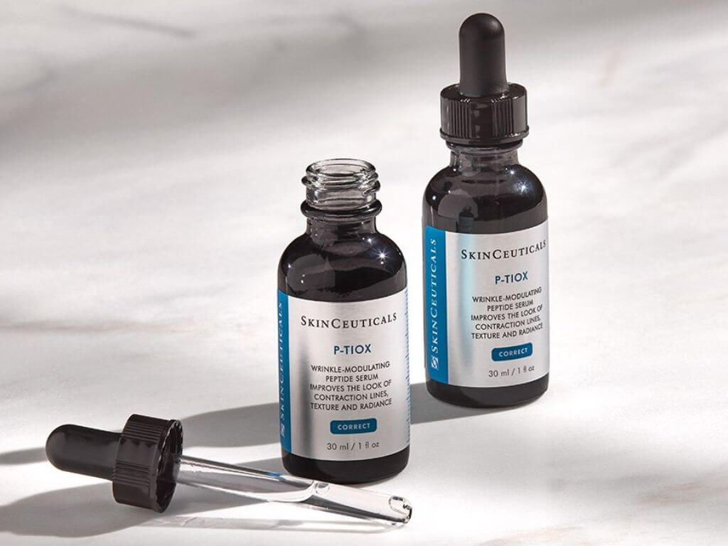 A photograph of two bottles of SkinCeuticals P-TIOX wrinkle-modulating peptide serum displayed on a marble surface.