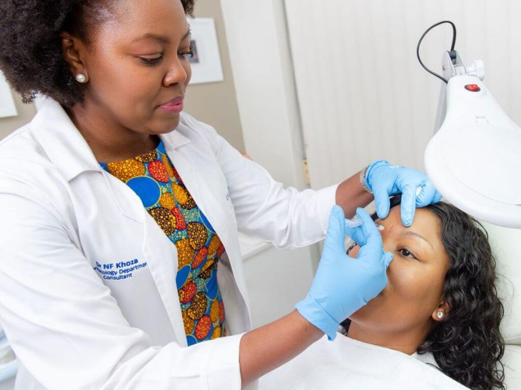 Dr. Nokubonga Khoza wearing gloves performing a skincare treatment on a patient.