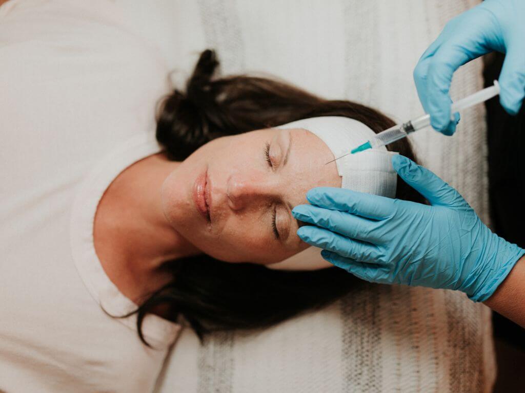 A medical professional wearing gloves administering a facial injection to a patient.