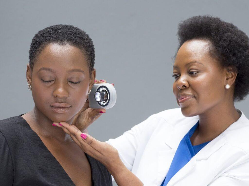 Dr. Nokubonga Khoza examining a patient's skin using a magnifying device, focusing on a detailed skin analysis.