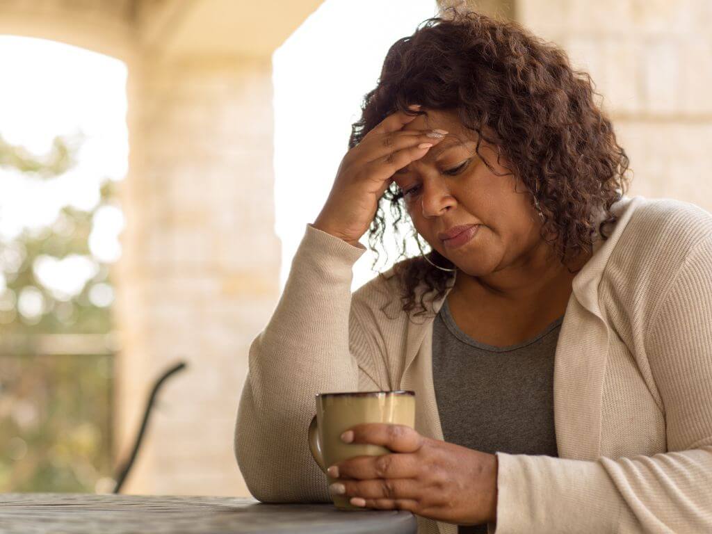 Middle-aged African woman holding a cup and reflecting on menopause skin changes and fatigue.