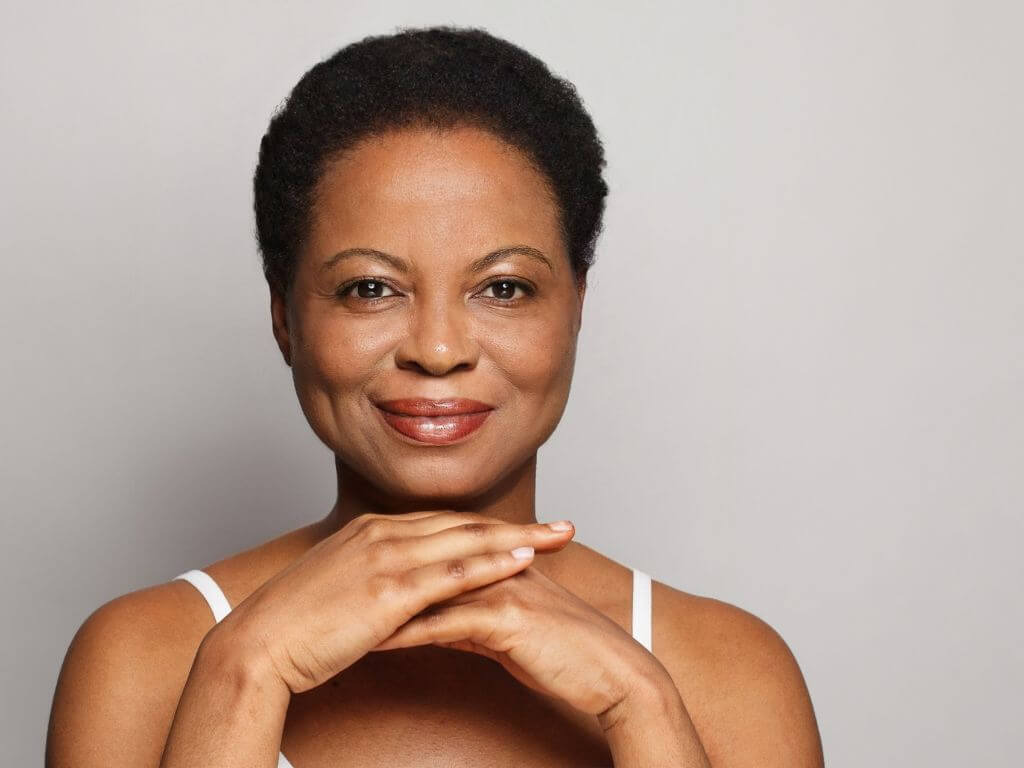 Confident mature African woman smiling after professional treatment for menopause skin changes.